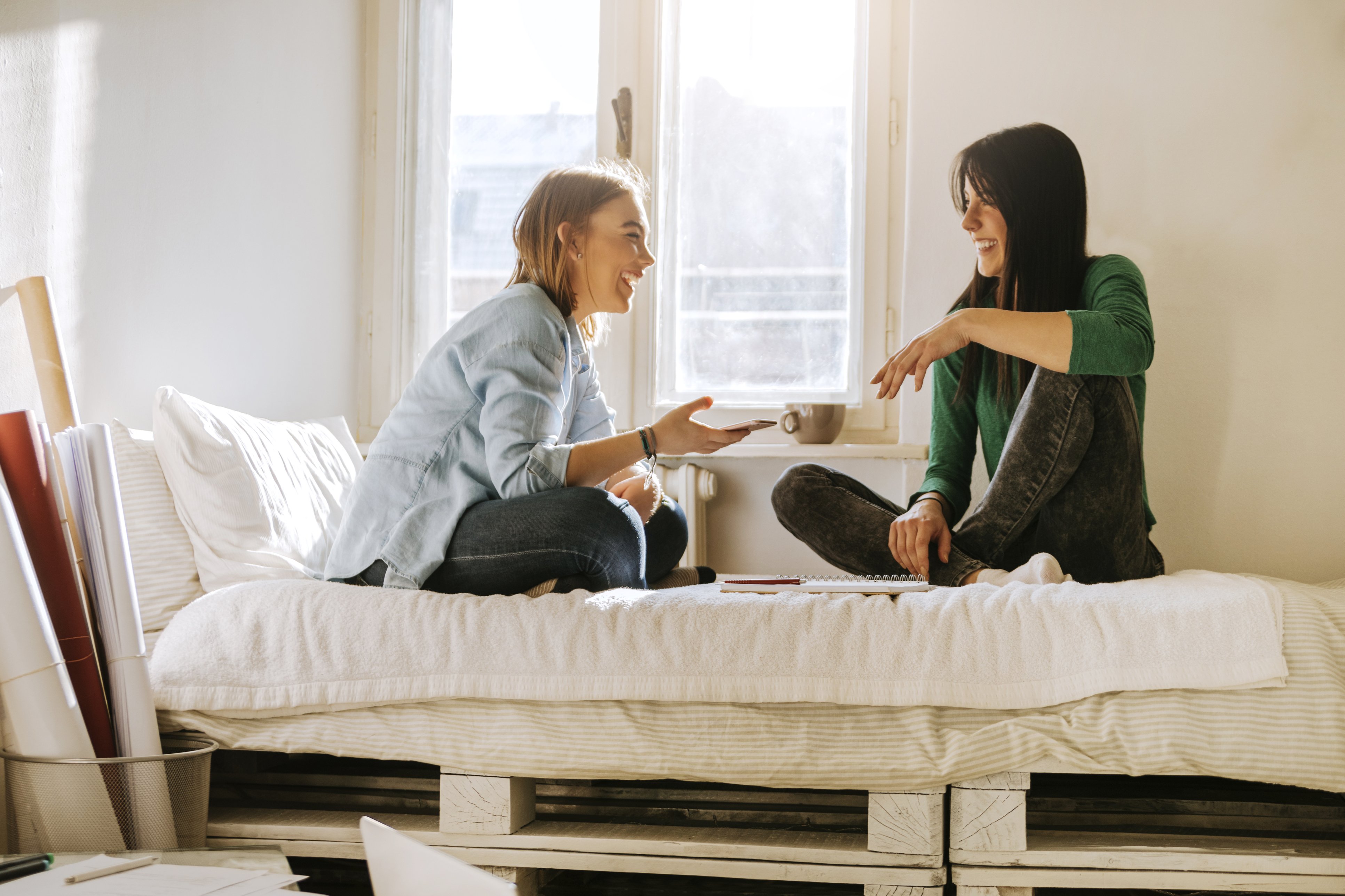 zwei Studentinnen sitzen auf einem Bett und unterhalten sich 