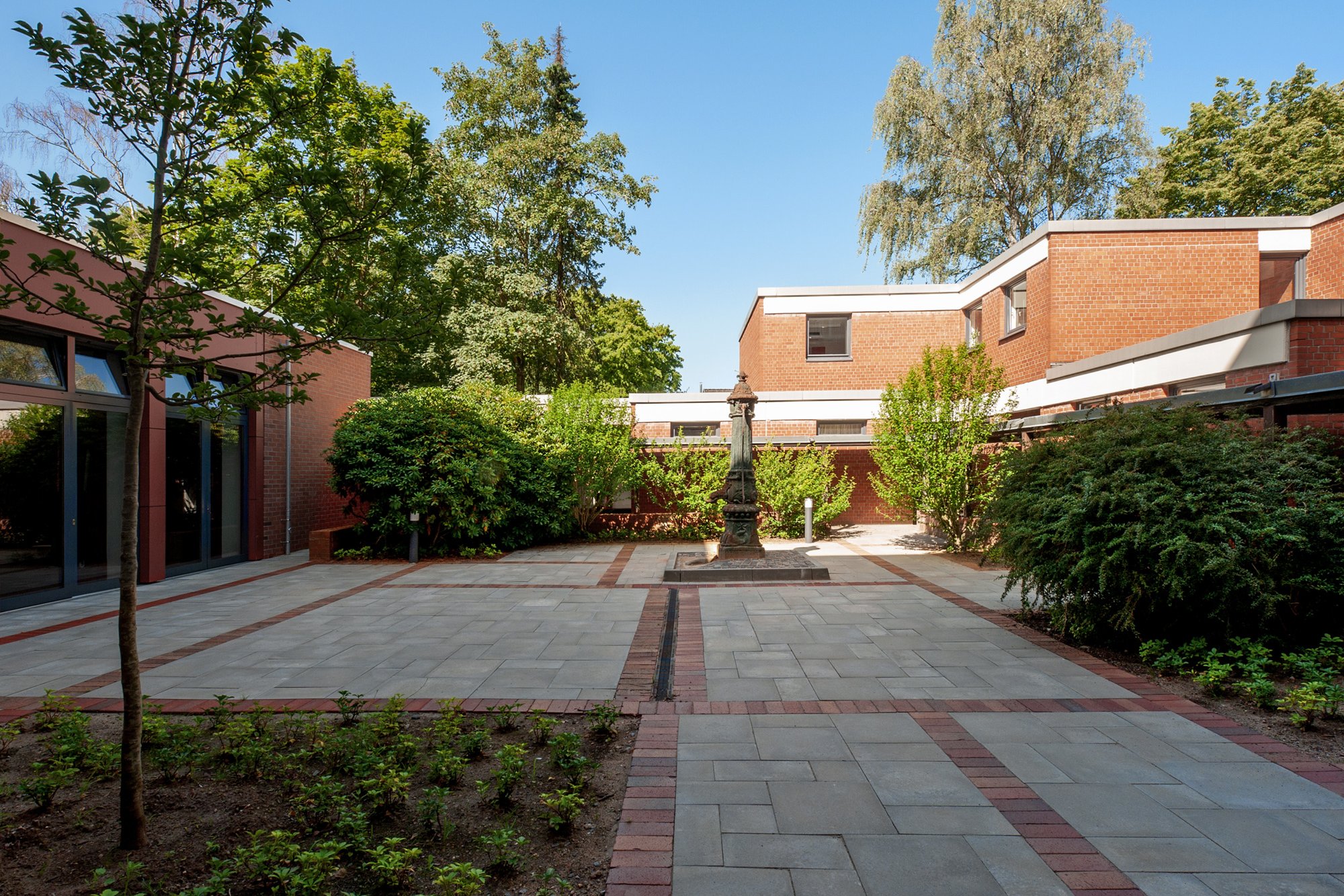 Innenhof mit Büschen, Bäumen und gepflasterem Weg der Wohnanlage Esther-Bejarano-Haus