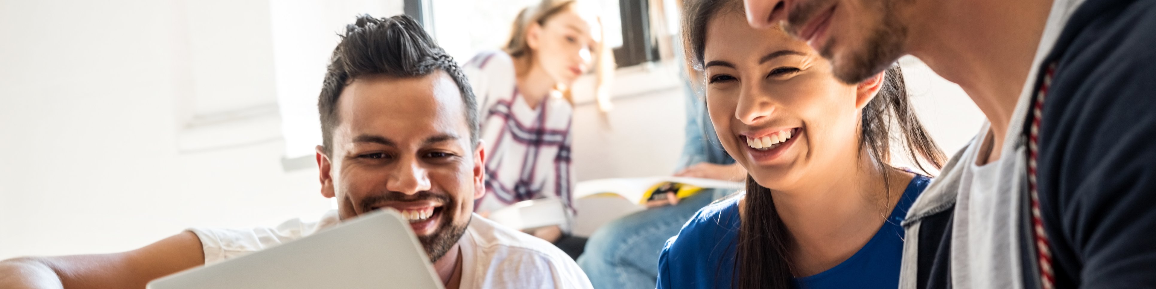 Three students sit next to each other and look at a tablet.