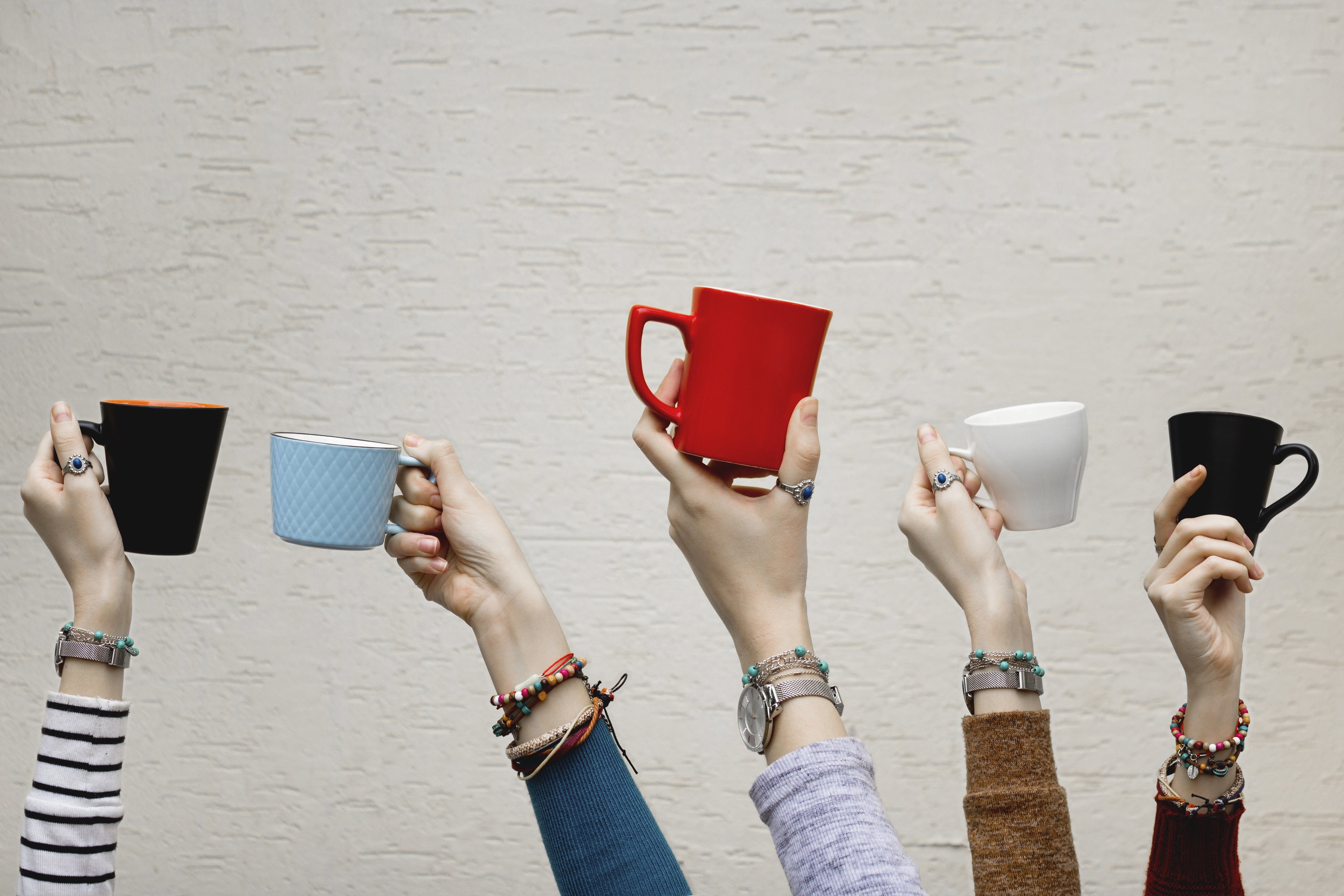 Fünf Hände halten jeweils eine Tasse in die Luft Fünf Hände halten jeweils eine Tasse in die Luft