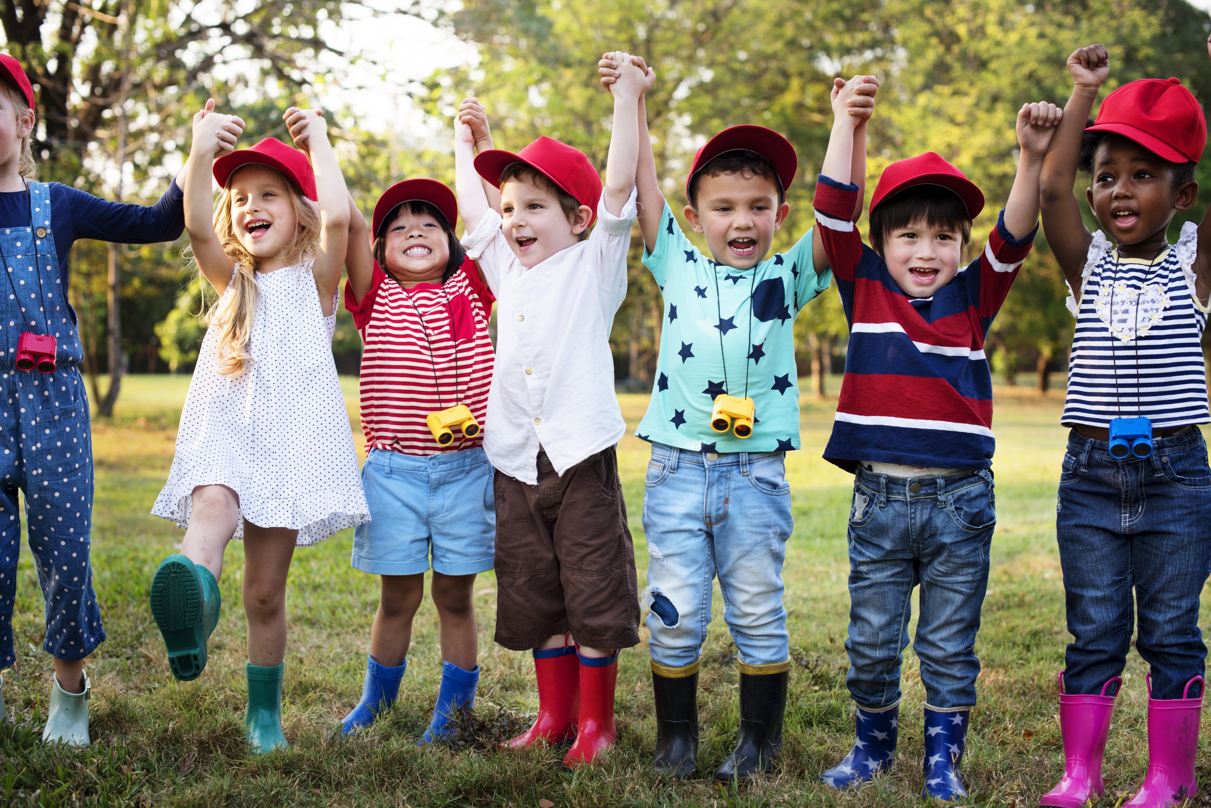 Gruppe von Kindergartenkindern, Hand in Hand, heben Arme fröhlich hoch 