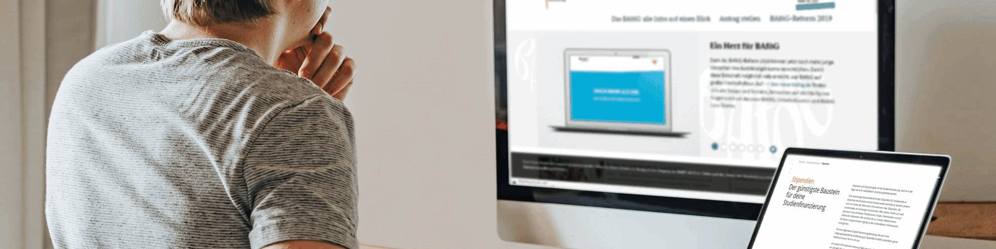 Junger Mann sitzt vor seinem PC und Laptop am Schreibtisch