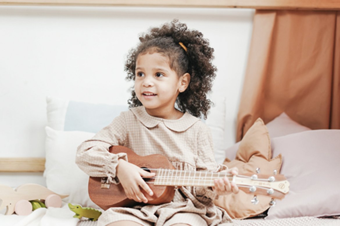 Little girl playing a small guitar while sitting down.